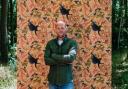 Tamlyn Blasdale-Holmes in front of a panel of his Raven Harvest wallpaper.