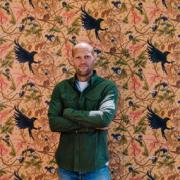 Tamlyn Blasdale-Holmes in front of a panel of his Raven Harvest wallpaper.